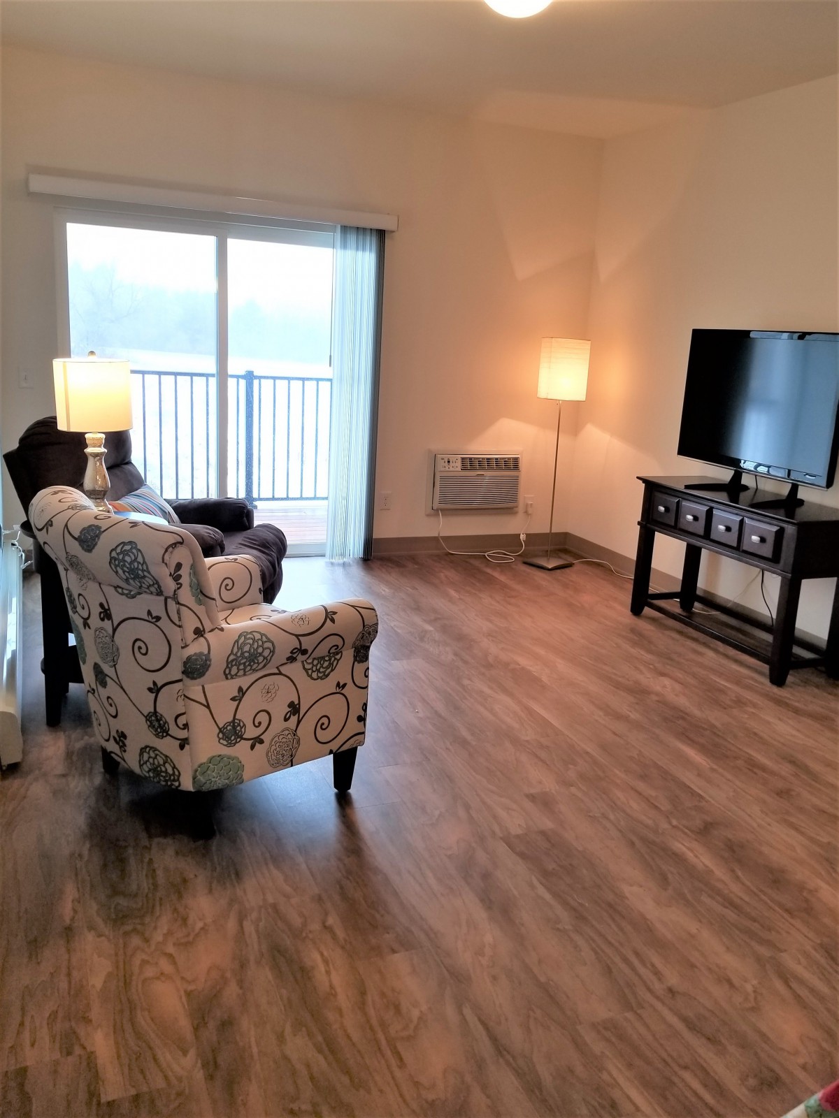 A cozy living room with chairs, lamps, a TV, and wood flooring.