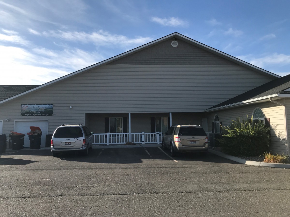 A simple building with two parked vehicles in front, under a clear blue sky.