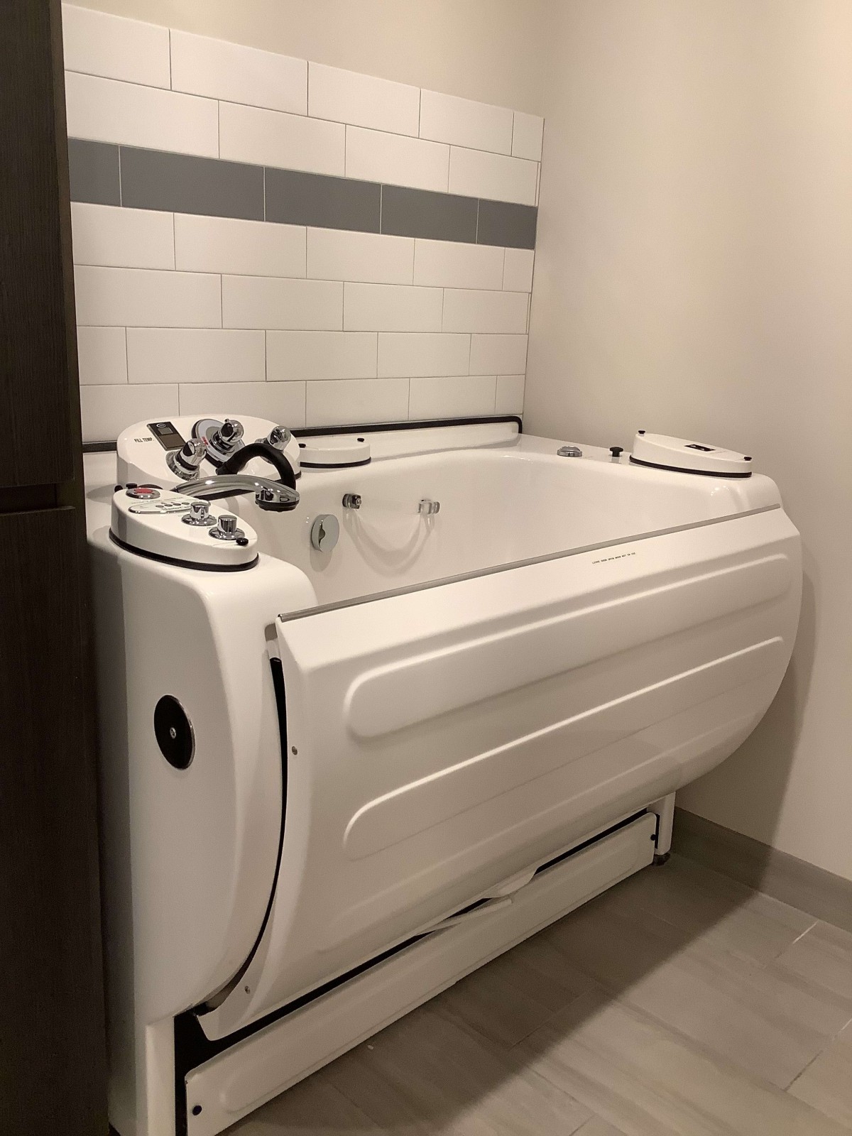 A modern, white walk-in bathtub in a tiled bathroom designed for accessibility.