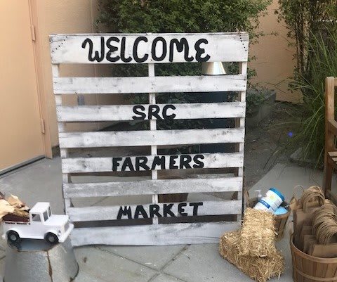 Welcome sign for the SRC Farmers Market displayed on a wooden pallet.