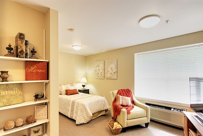 A cozy bedroom with soft lighting, featuring a neatly made bed, an armchair draped with a blanket, and tasteful decor.