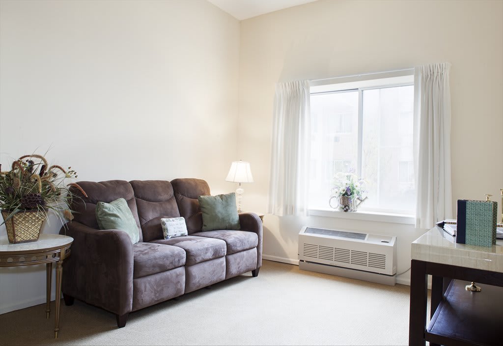 A cozy living room with a brown sofa, decorative cushions, and a lamp beside a large window.