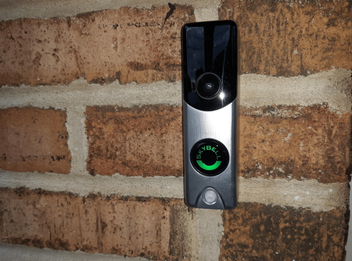 A modern video doorbell installed on a brick wall.