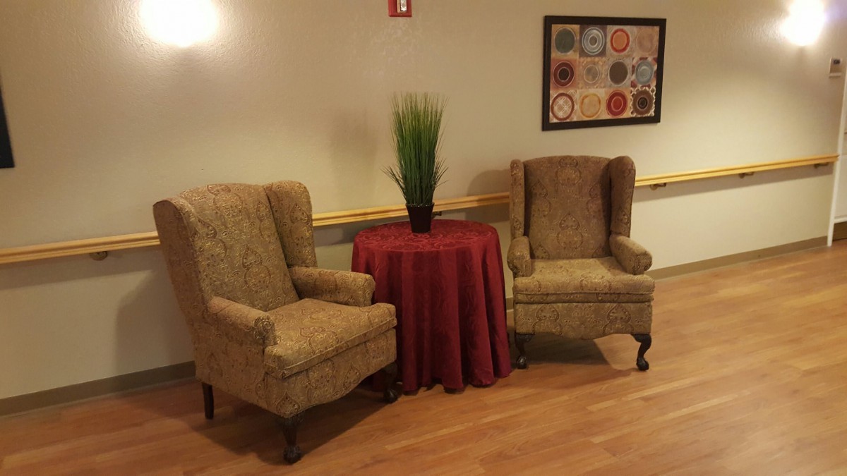 A cozy seating area with two armchairs, a small table covered with a red cloth, and a potted plant.