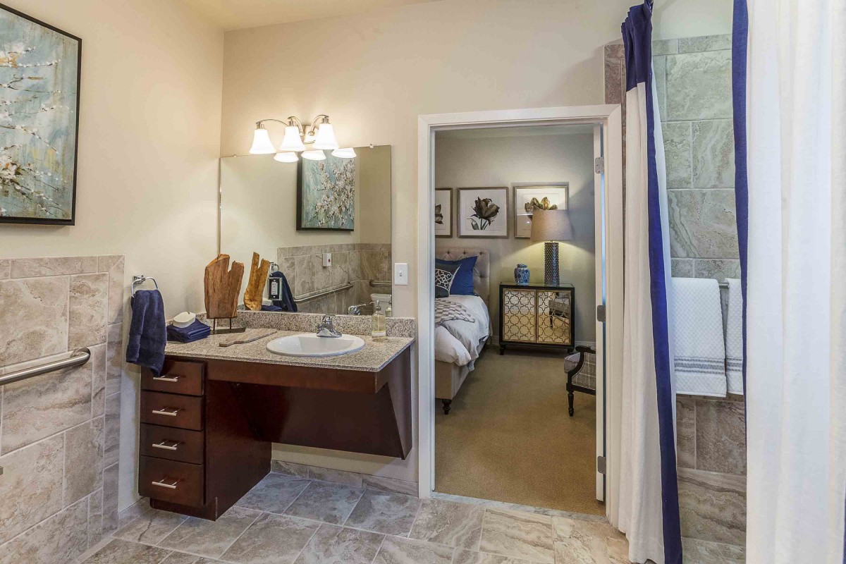A view from a bathroom looking into a well-decorated bedroom, featuring a modern vanity and warm lighting.