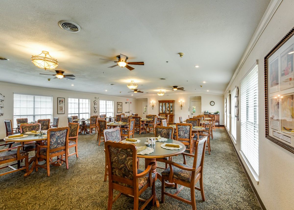 An inviting dining room with multiple tables and chairs, featuring ceiling fans and natural lighting from large windows.