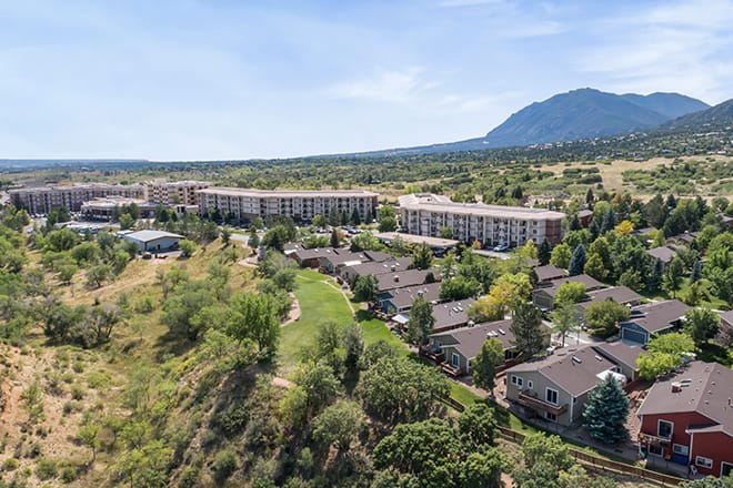Aerial view of a residential area with buildings, surrounded by lush greenery and mountains in the background.