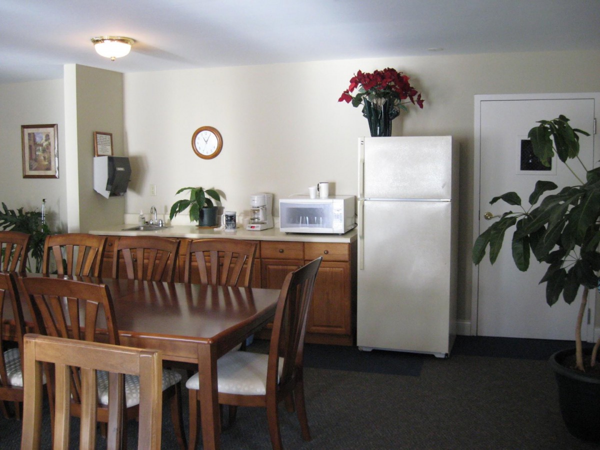 A cozy kitchen and dining area with a wooden table and chairs, a refrigerator, and decorative plants.
