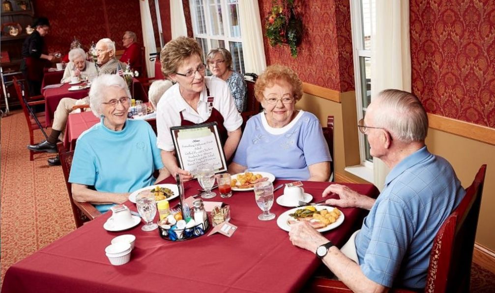 A group of seniors enjoying a meal at a restaurant, served by a waitress.