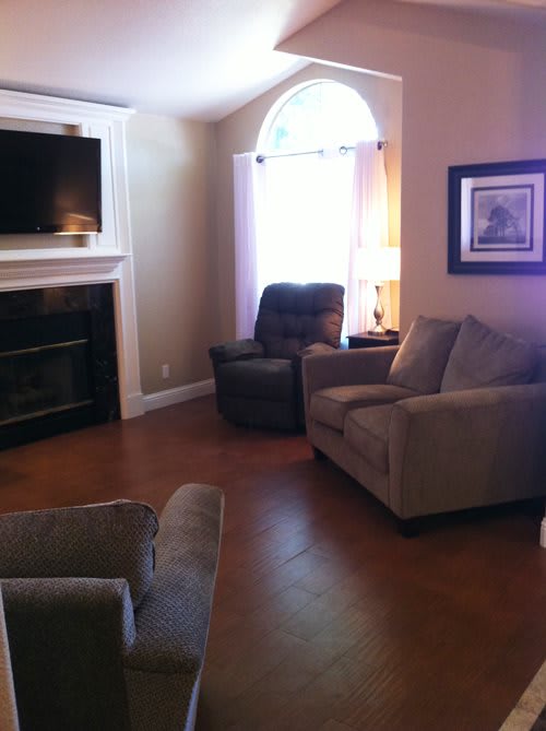 A cozy living room with sofas, armchairs, and a fireplace, featuring a television mounted above.