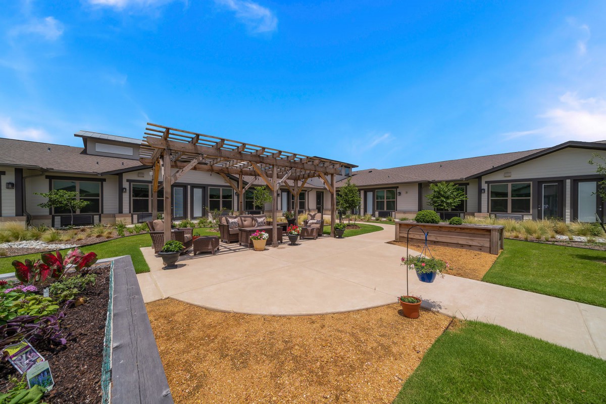 A well-maintained courtyard featuring a pergola with outdoor seating and landscaped gardens under a clear blue sky.