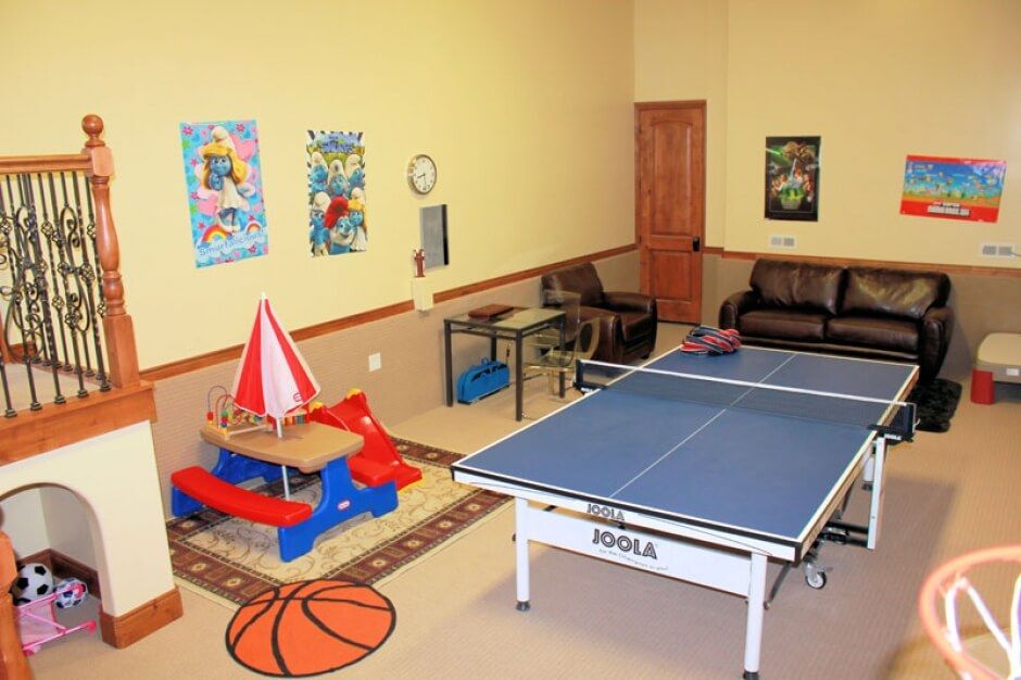 A colorful playroom featuring a table tennis setup, children's toys, and seating area with decorative posters on the wall.