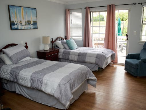A cozy bedroom with twin beds, soft curtains, and a view outside.