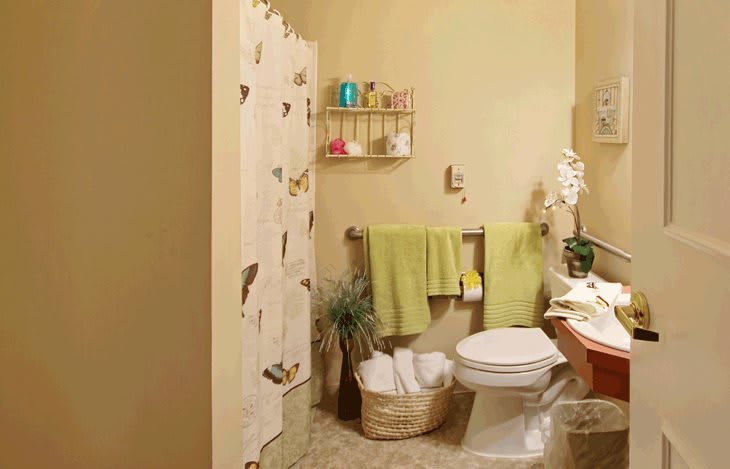 A neatly organized bathroom with green towels and a floral shower curtain.