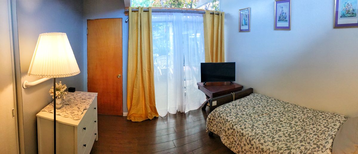 A cozy bedroom with a bed, television, and large window with yellow curtains.