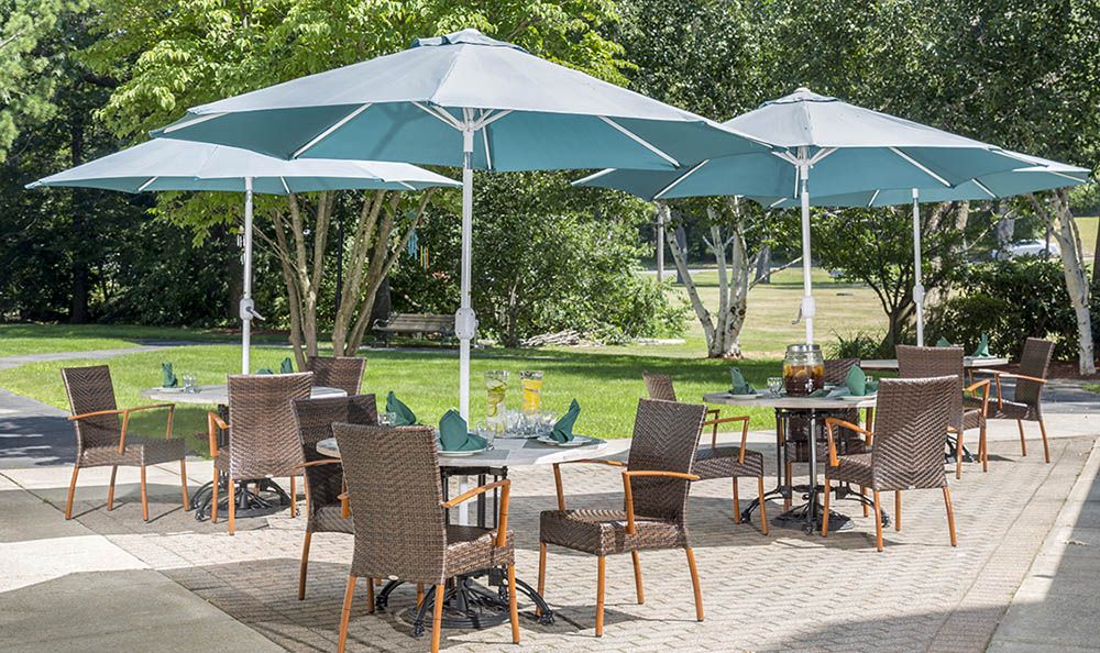An outdoor patio area with tables, chairs, and umbrellas in a garden setting.