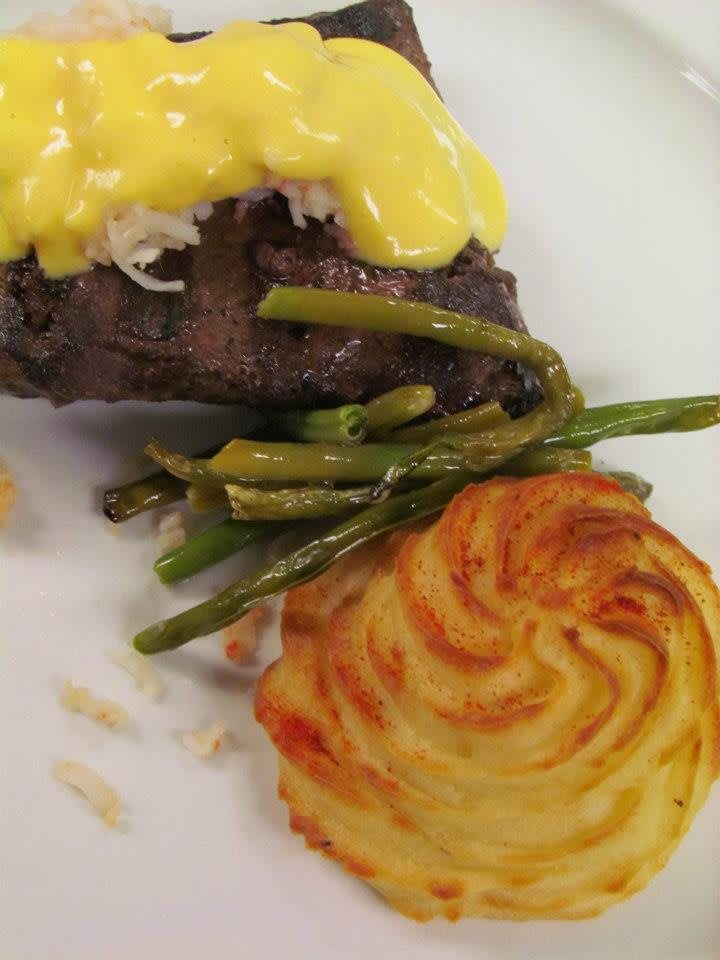 A gourmet dish featuring steak topped with hollandaise sauce, served with asparagus and a swirl of baked potato.