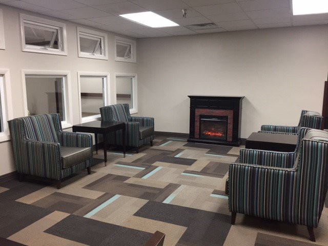 A cozy lounge area with striped chairs, a fireplace, and large windows.
