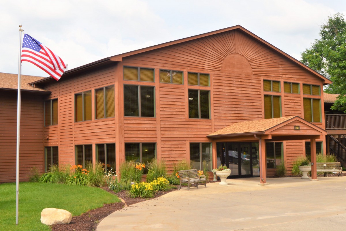 A wooden office building with a flag and landscaped surroundings.