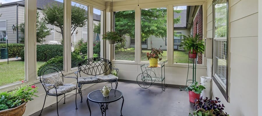A cozy sunroom with wrought iron furniture and potted plants, bathed in natural light.
