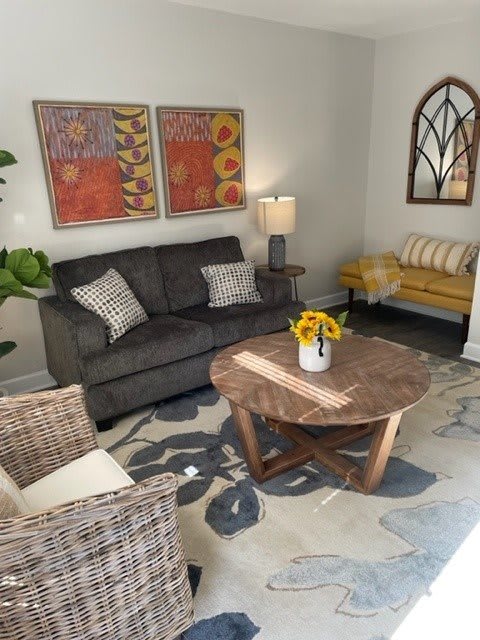A cozy and modern living room featuring a gray sofa, wicker chair, wooden coffee table, colorful artwork, and decorative accents.