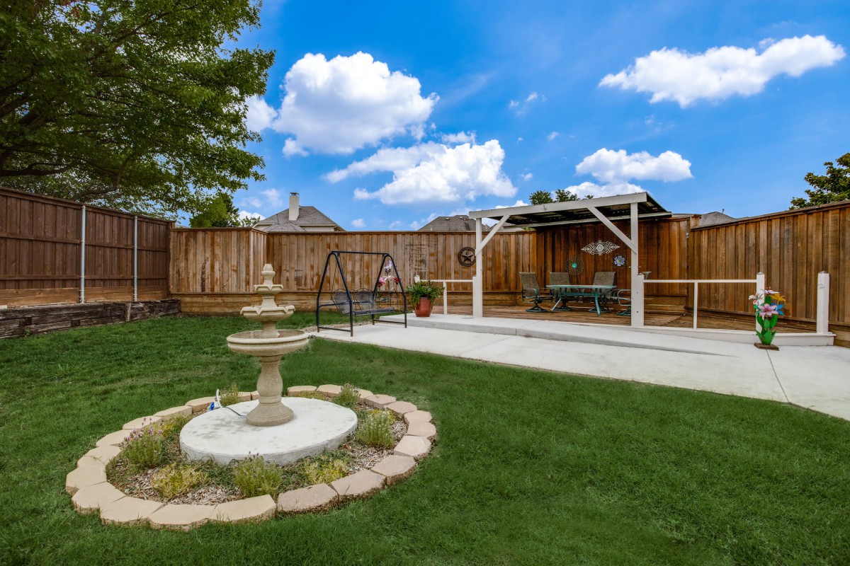 A serene backyard featuring a fountain, swing, and pergola on a sunny day.