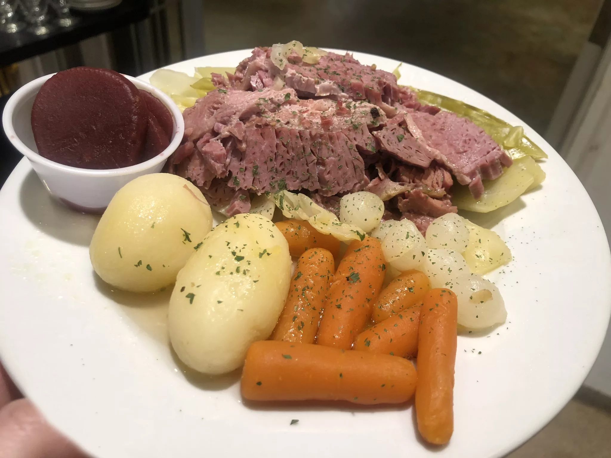 A plate of corned beef with boiled potatoes, carrots, pearl onions, and a side of beets.
