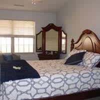 A cozy bedroom with a large bed, patterned bedding, and a wooden dresser with a mirror.