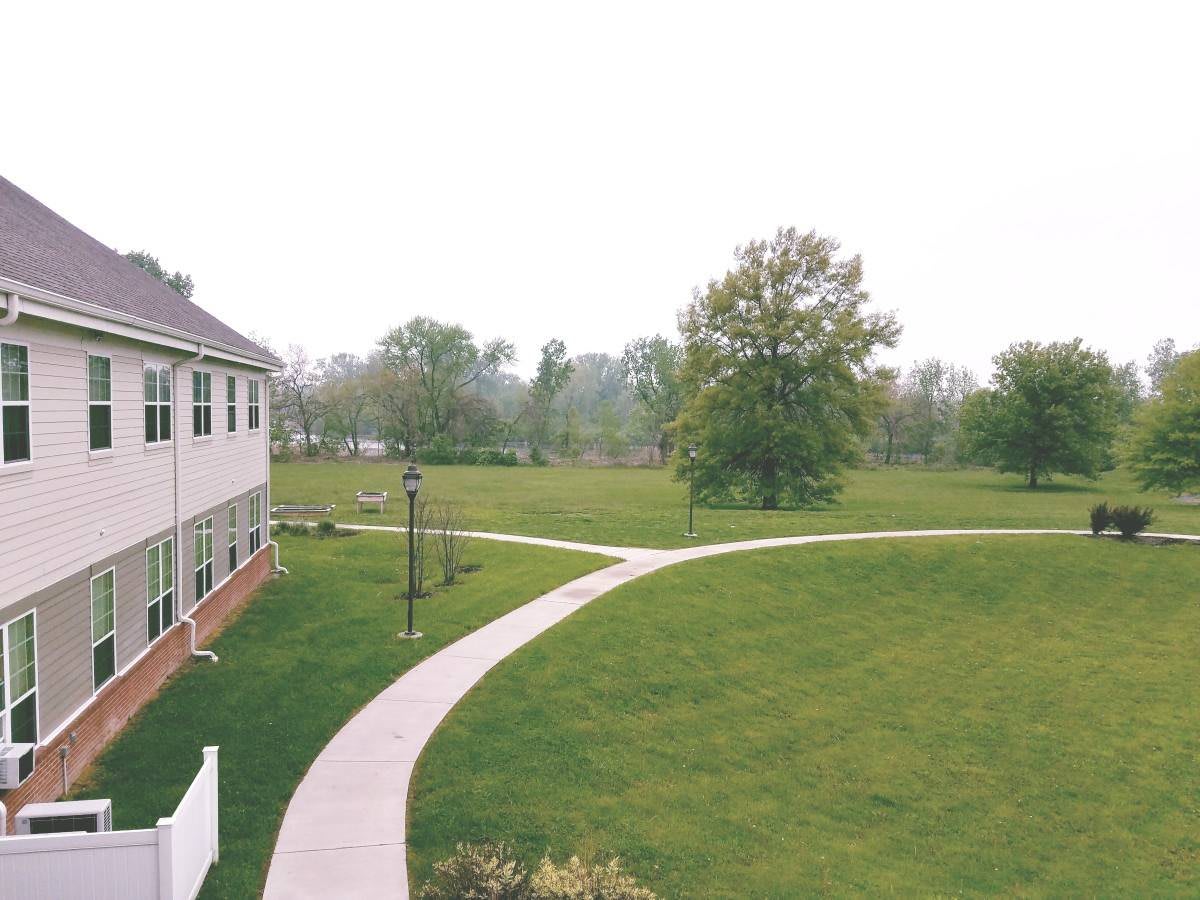 A scenic view of a building with a pathway curving through a grassy area surrounded by trees.