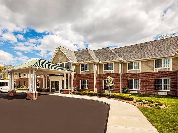 A modern two-story brick building with a covered entrance and landscaped surroundings under a cloudy sky.