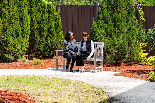 Two individuals engaged in a heartfelt conversation on a park bench surrounded by lush greenery.