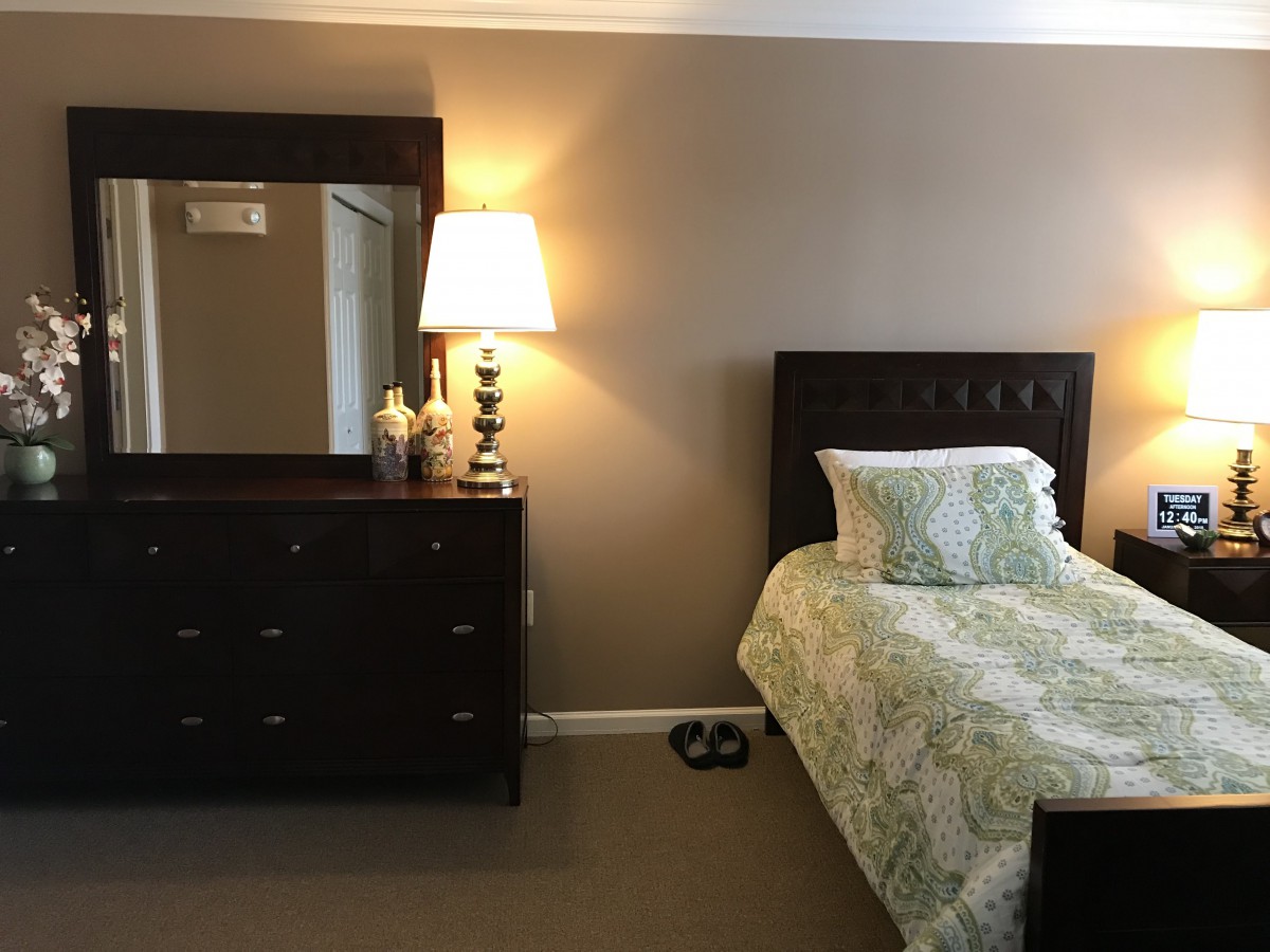 A cozy bedroom with a single bed, dresser, and lamp.