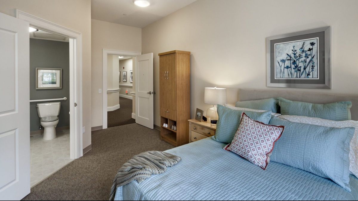 A cozy bedroom with a neatly made bed, a wooden wardrobe, and a bedside lamp.