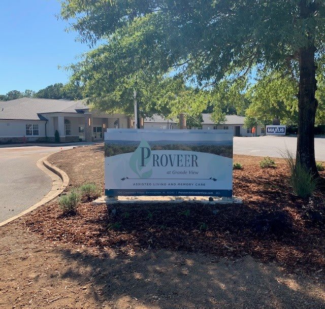 An outdoor sign in front of a professional office building surrounded by trees.