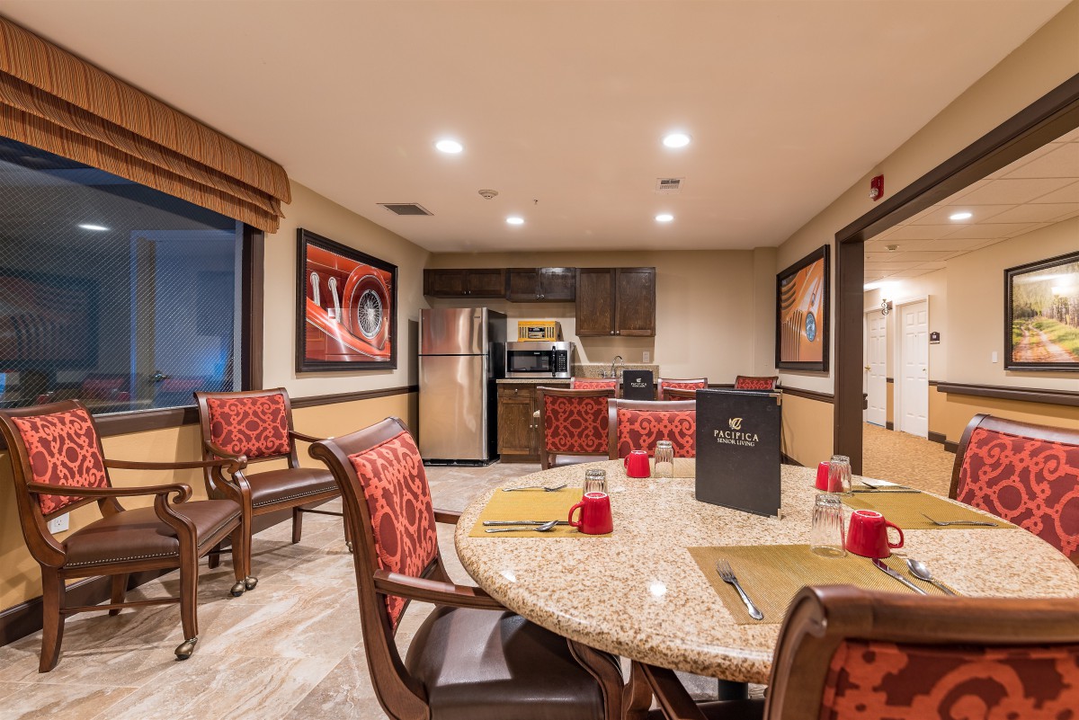 A modern and cozy dining area connected to a kitchen, featuring a round table set for dinner and decorated with colorful artwork.