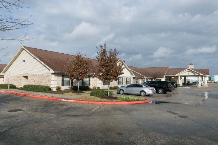 A suburban building with a parking lot and several cars parked under a cloudy sky.