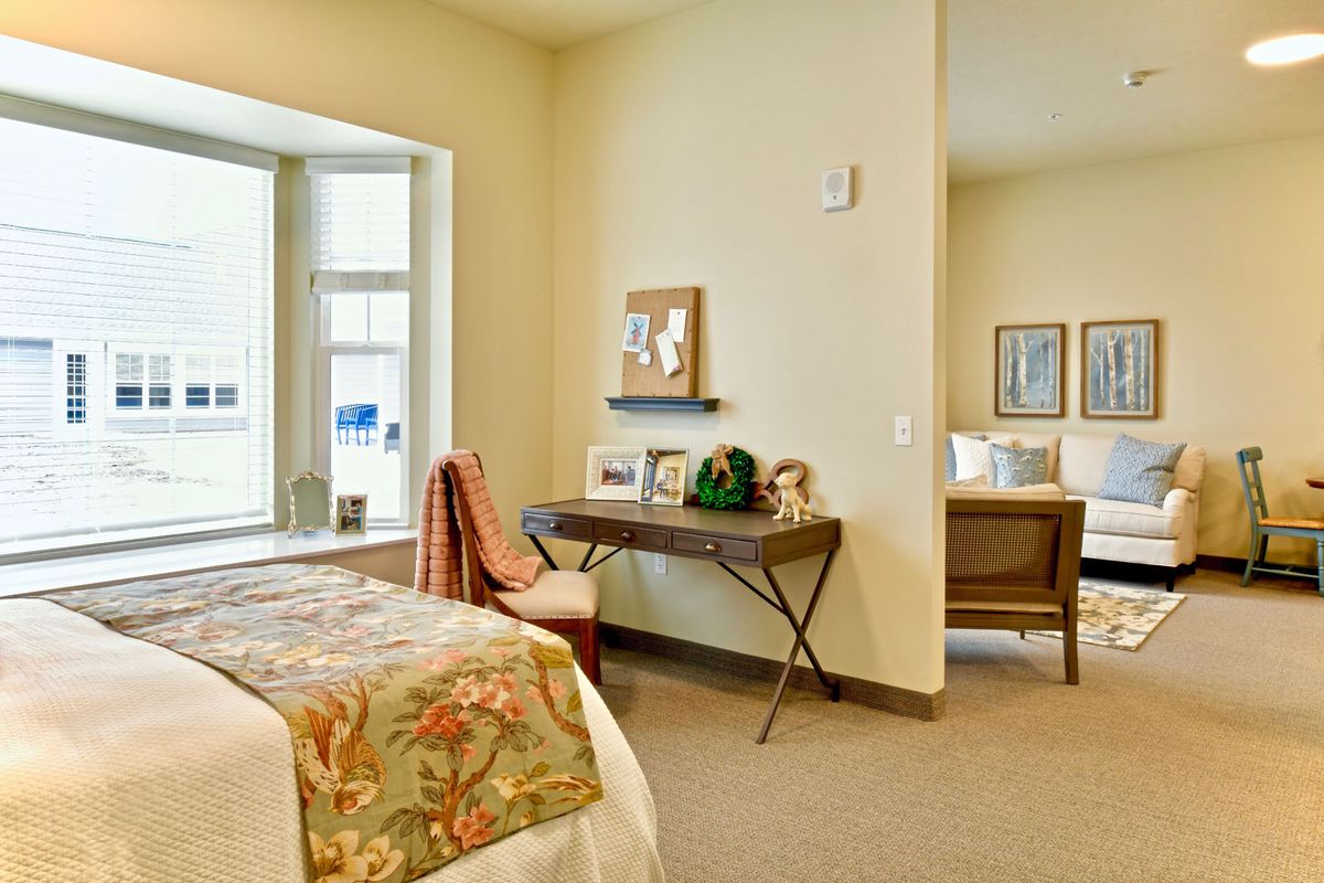 A cozy bedroom featuring a decorative bedspread, a small desk with artwork, and natural lighting.