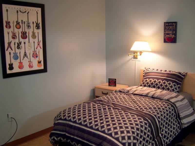 A cozy bedroom with patterned bedding, a wall-mounted lamp, and guitar-themed artwork.