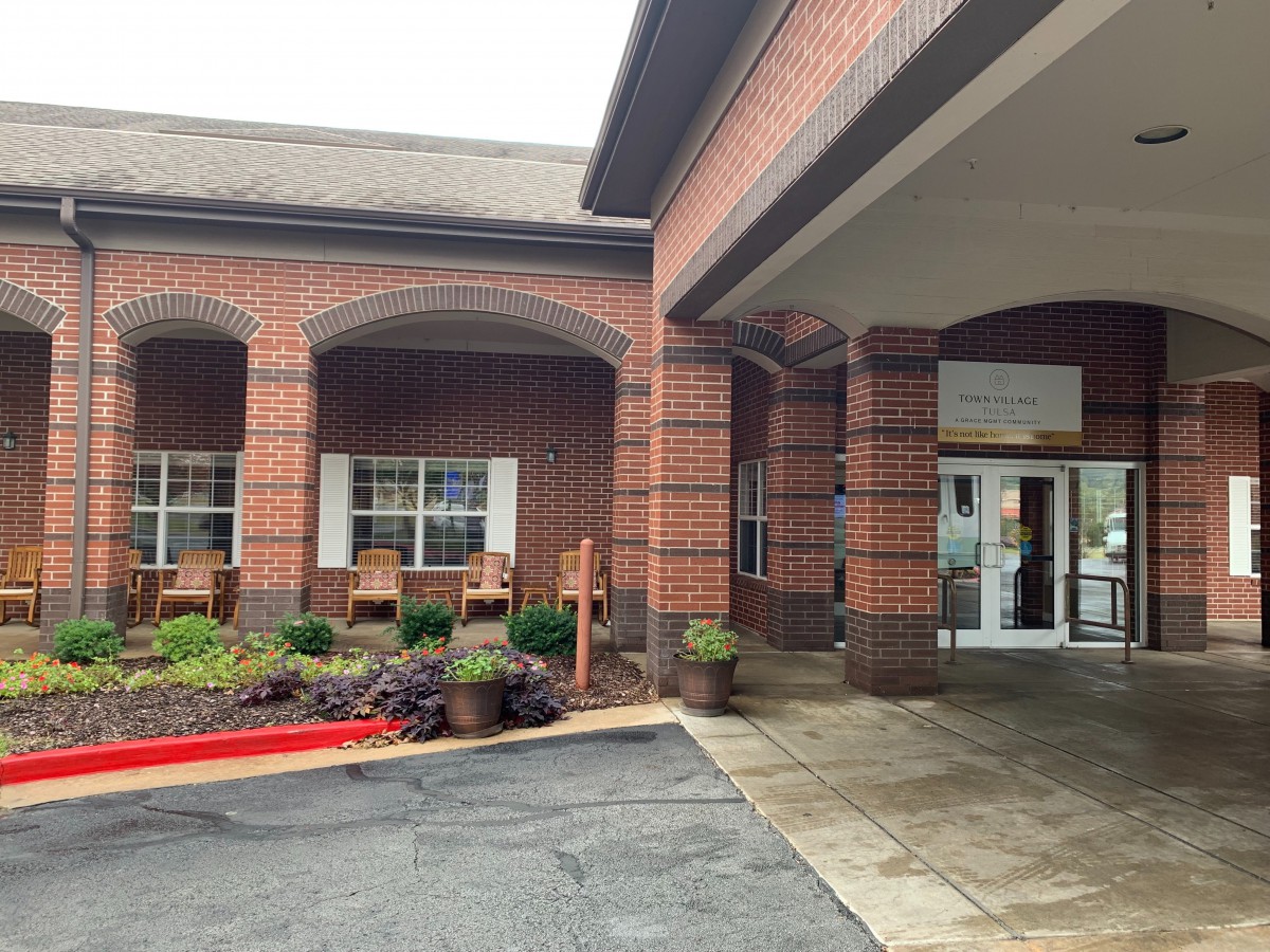 A brick building entrance with a covered walkway, featuring outdoor seating and landscaping.