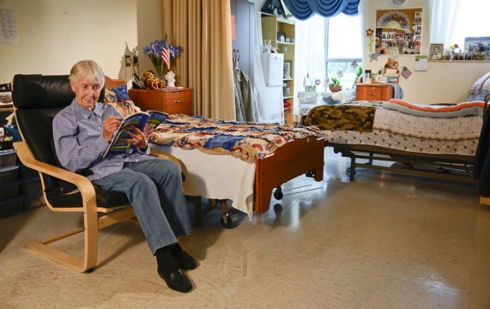 An elderly person is sitting in a cozy nursing home room, reading a book.