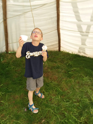 A young boy joyfully enjoying ice cream inside a tent.