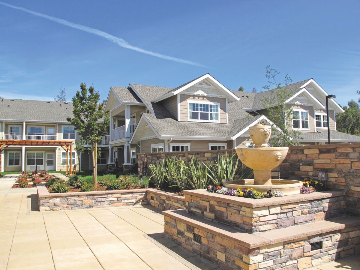 A beautiful house with a stone fountain and landscaped surroundings on a sunny day.