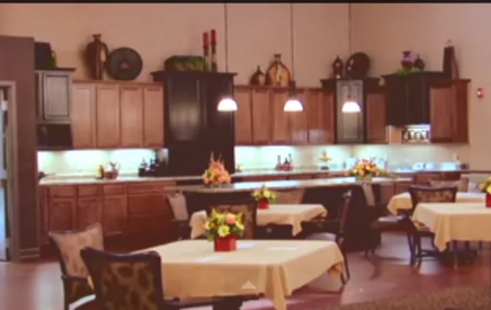 A cozy kitchen interior with tables and chairs, decorated with flowers and warm lighting.