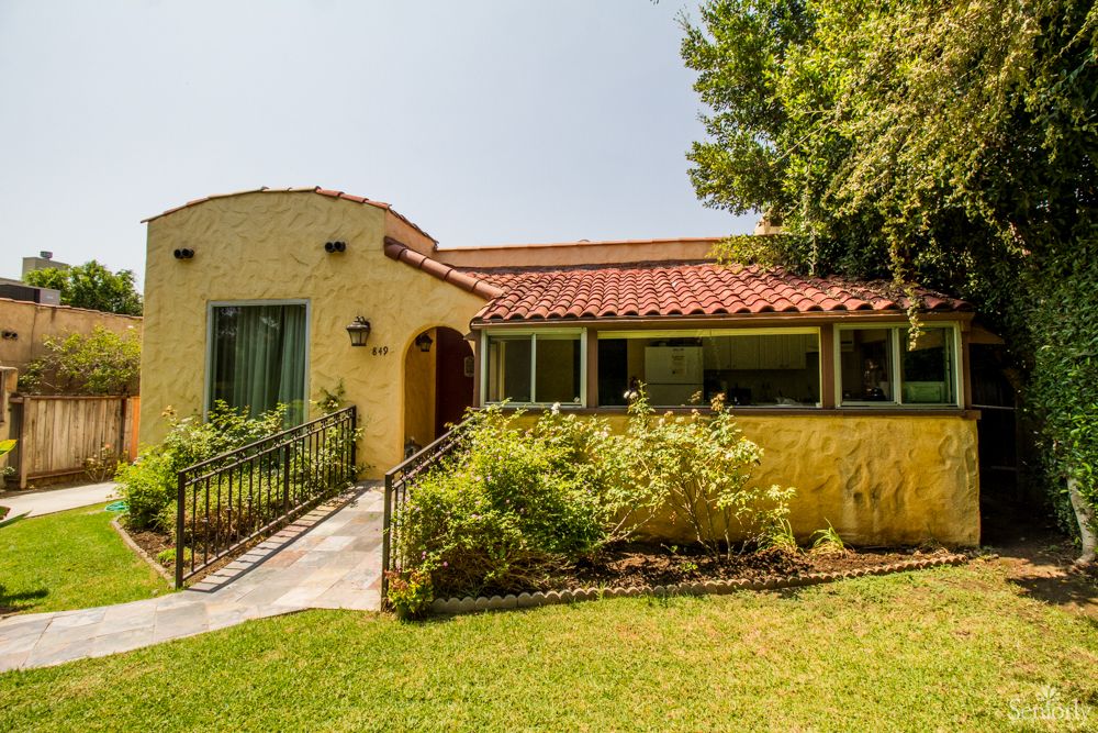 A charming single-story house with a tiled roof, surrounded by lush greenery and a well-maintained garden.
