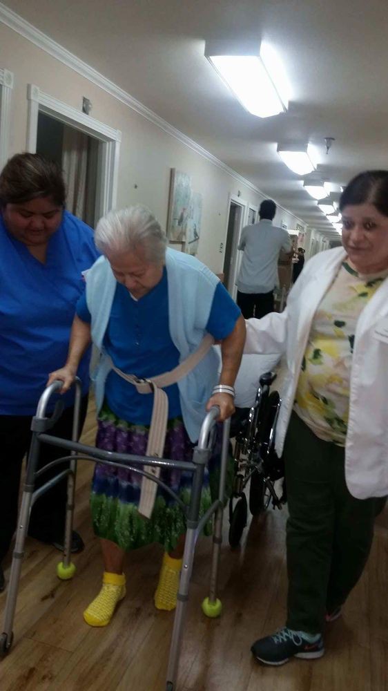 An elderly person receiving assistance from caregivers while using a walker in a nursing home.