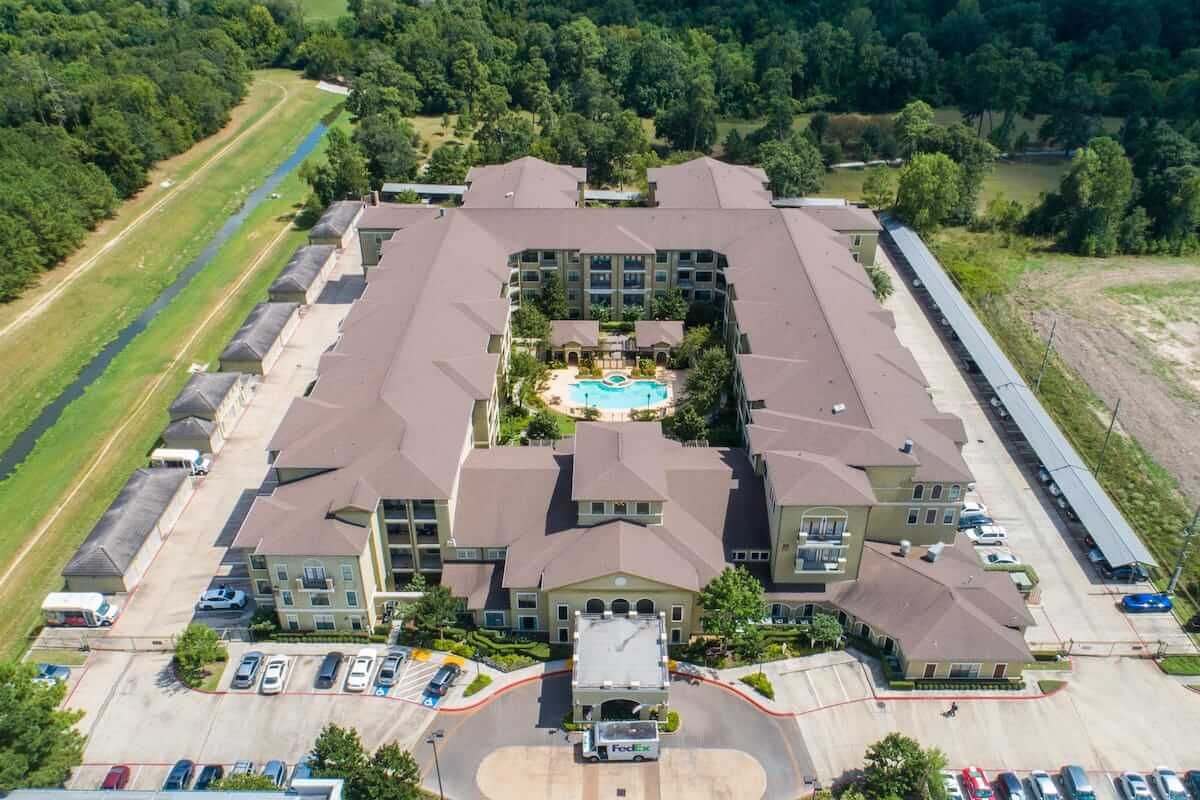 Aerial view of a residential complex with a central swimming pool, surrounded by greenery and parking areas.