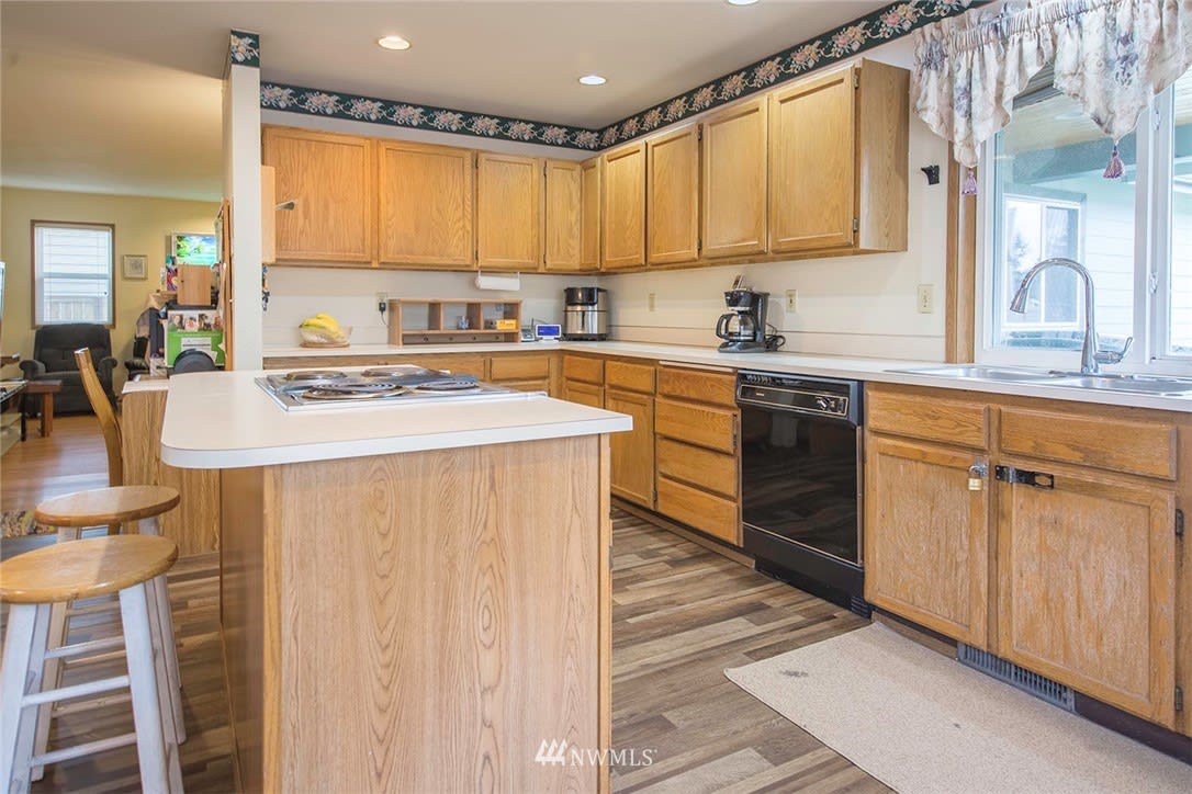 A modern kitchen with wooden cabinets and ample countertop space, featuring various appliances under natural lighting.