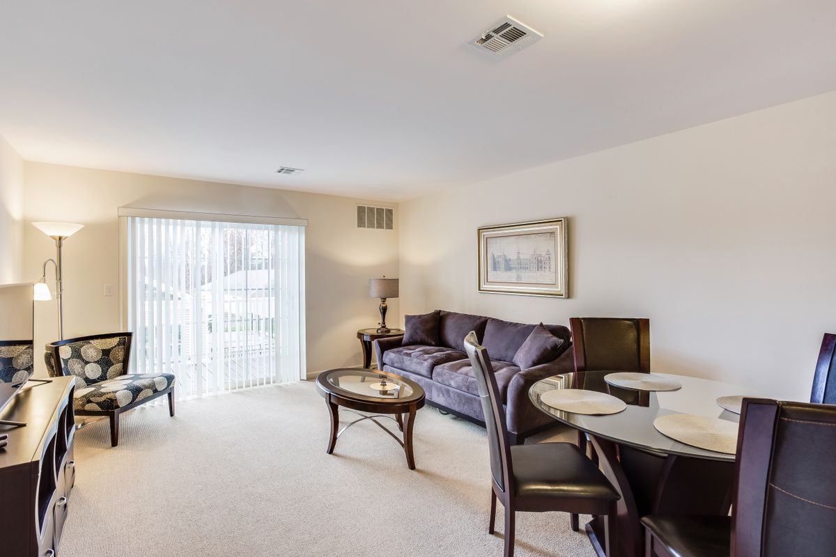 A modern living room with a sofa, coffee table, and dining area, featuring bright natural lighting.