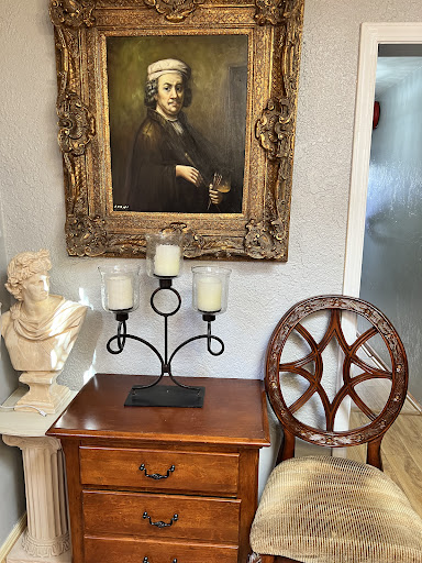 A vintage corner featuring a portrait, elegant chair, and decorative bust.