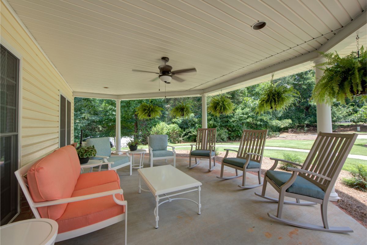 A cozy outdoor patio with cushioned seating, tables, and a ceiling fan overlooking a lush garden.
